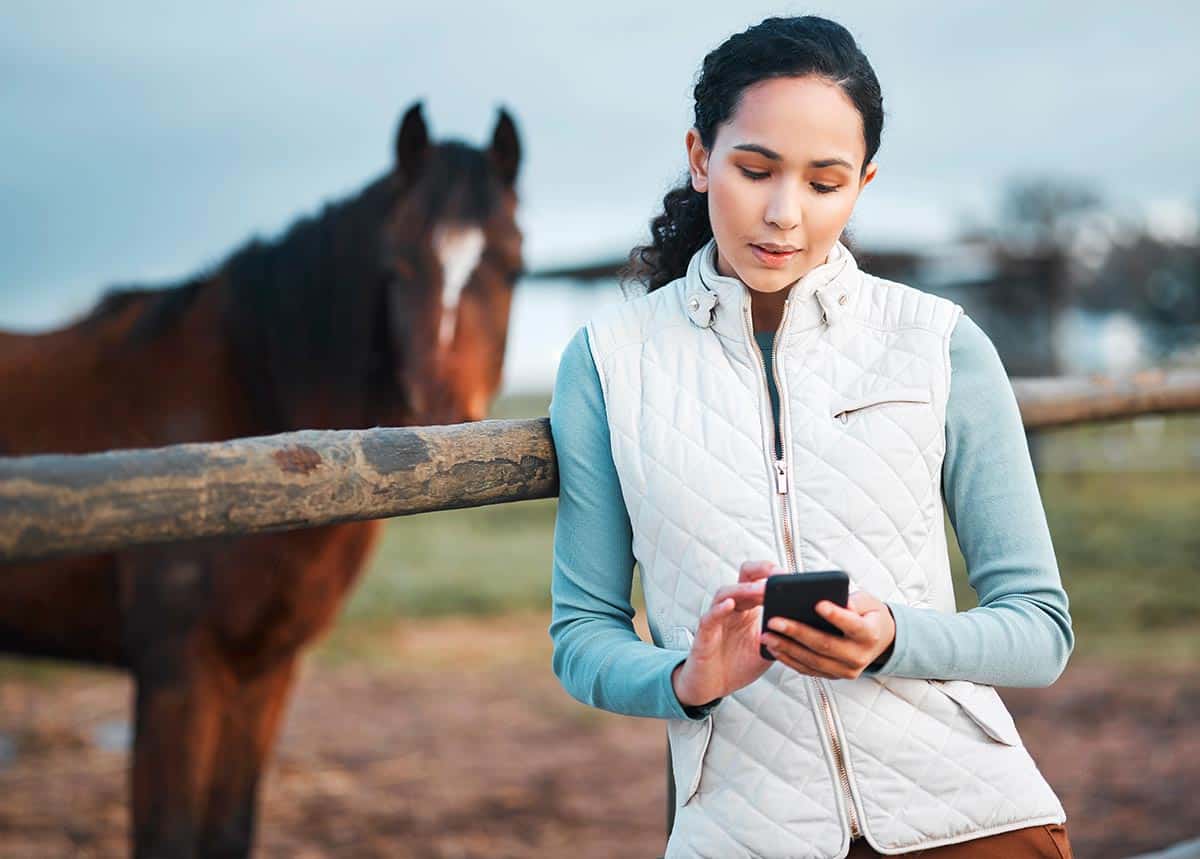 woman on phone with horse in background